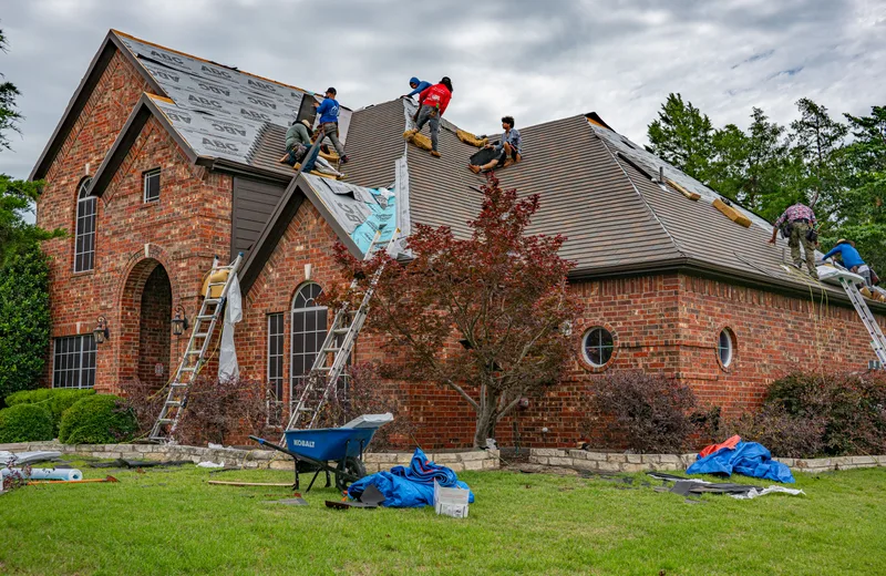 Roofing crew replacing shingles on a brick home